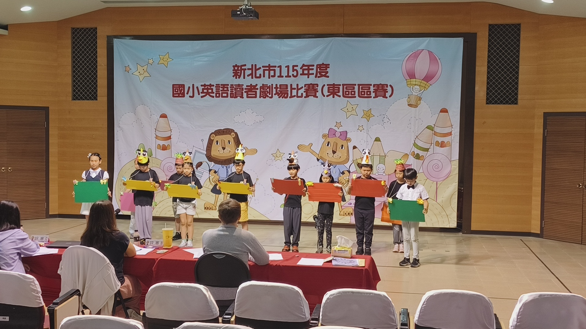 四年級參加英語讀者劇場比賽的現場狀況，有11個學生上台，胸前擺放用壓克力板做成的手稿來念