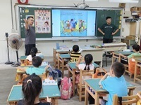 站在黑板的右邊為外師，左邊的中師伸出手來解釋，小孩乖乖的坐在位子聽故事